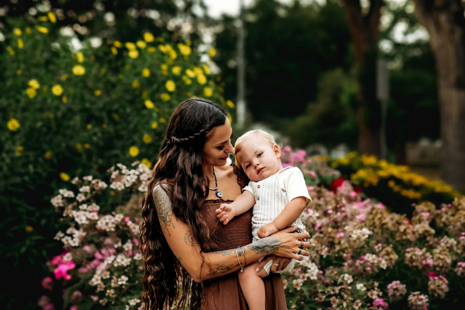 A tender moment between parent and child in a garden with blooming flowers and sunlit greenery.