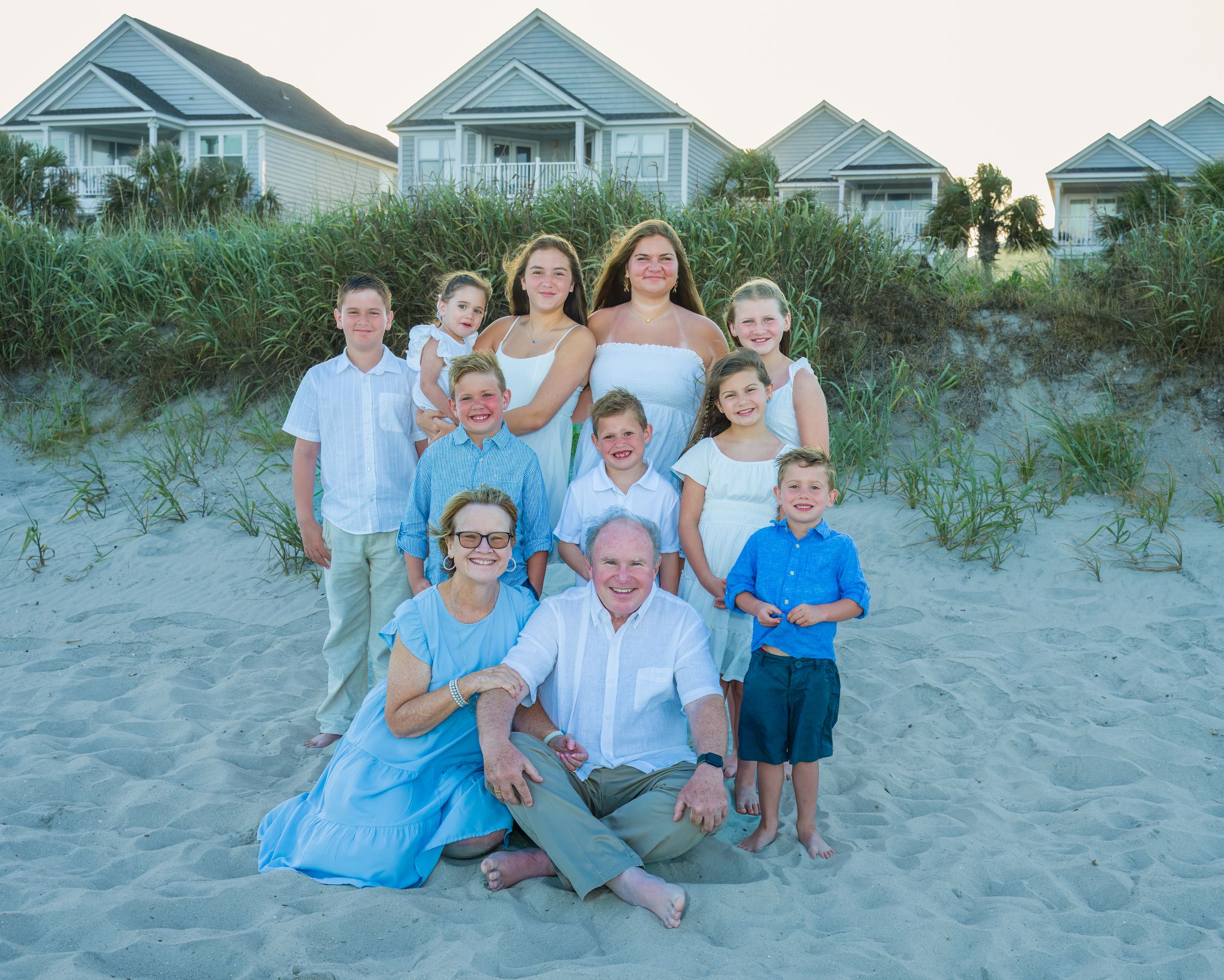 A series of family beach photos at sunset showing people sitting and posing together on sandy dunes near coastal homes.