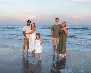 Group enjoying summer evening together on beach with waves and sunset in background at dusk.