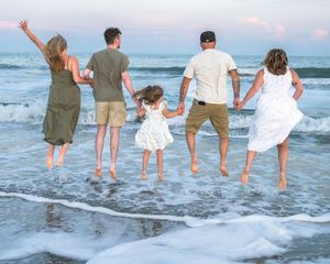 People holding hands and jumping together at sunset on a beach while ocean waves crash at their feet.