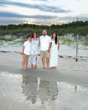 A group stands together on a sandy beach at sunset with dunes and vegetation in the background.