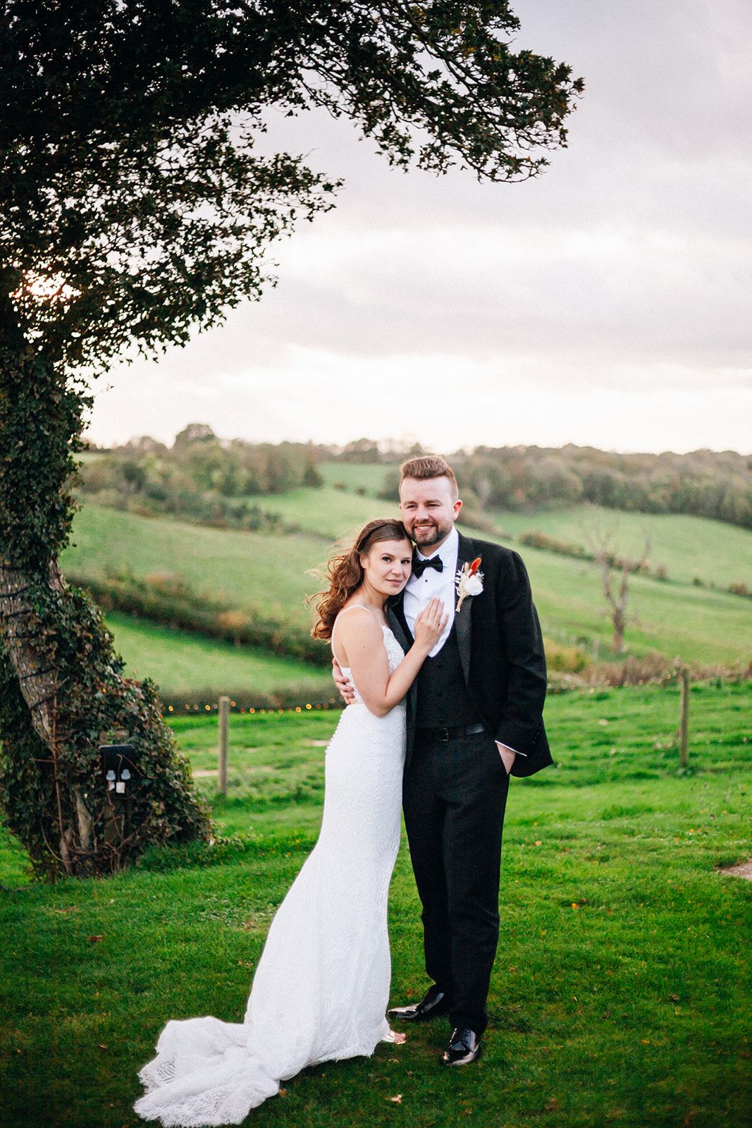 The Barn at Botley Hill - Bride & Groom share a romantic moment on a green hillside overlooking pastoral farmland.