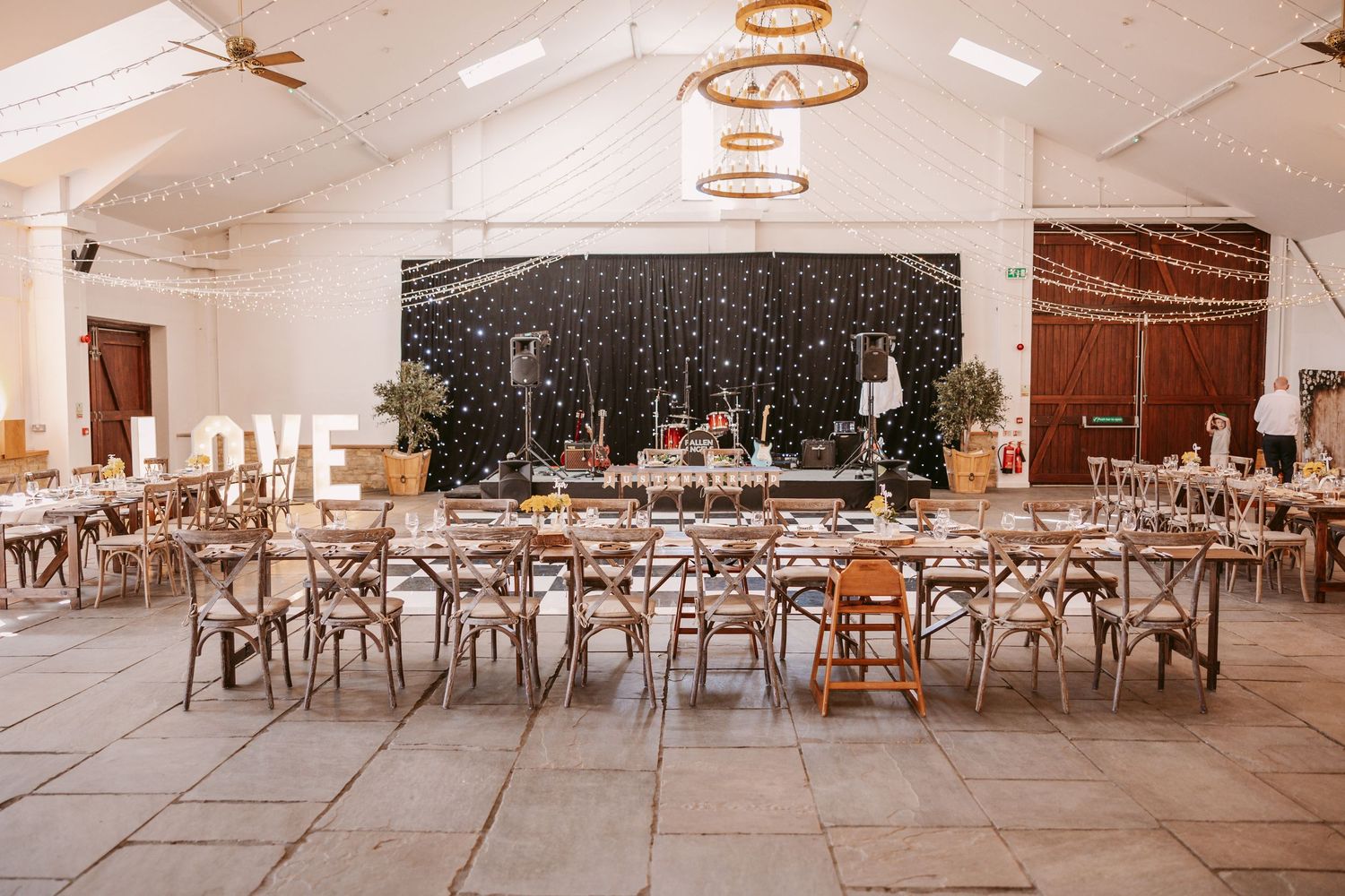 Wedding reception tables decorated with white linens and wooden chairs in an elegant indoor venue.