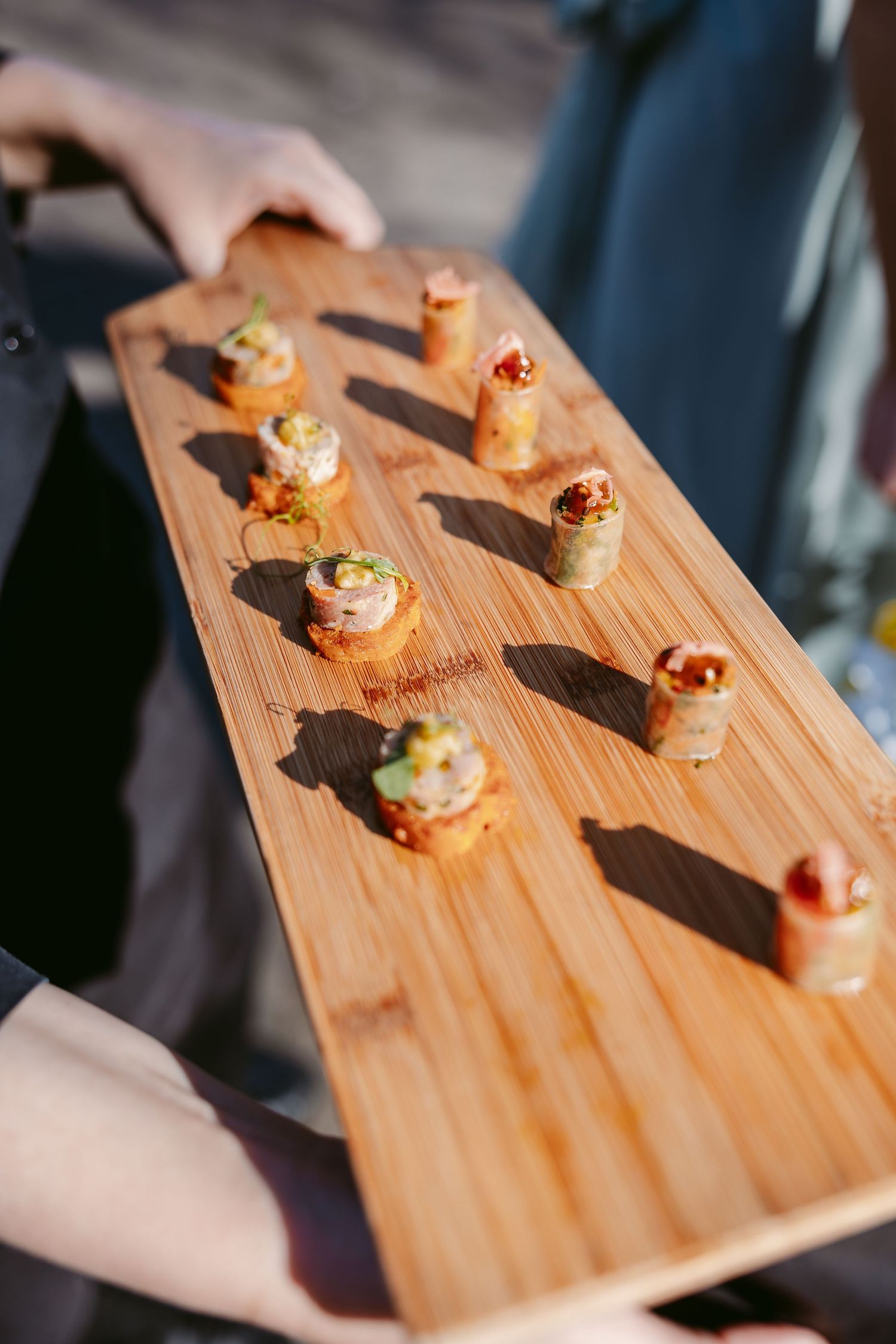 Elegant appetizers arranged on a wooden serving board casting dramatic shadows in natural lighting.