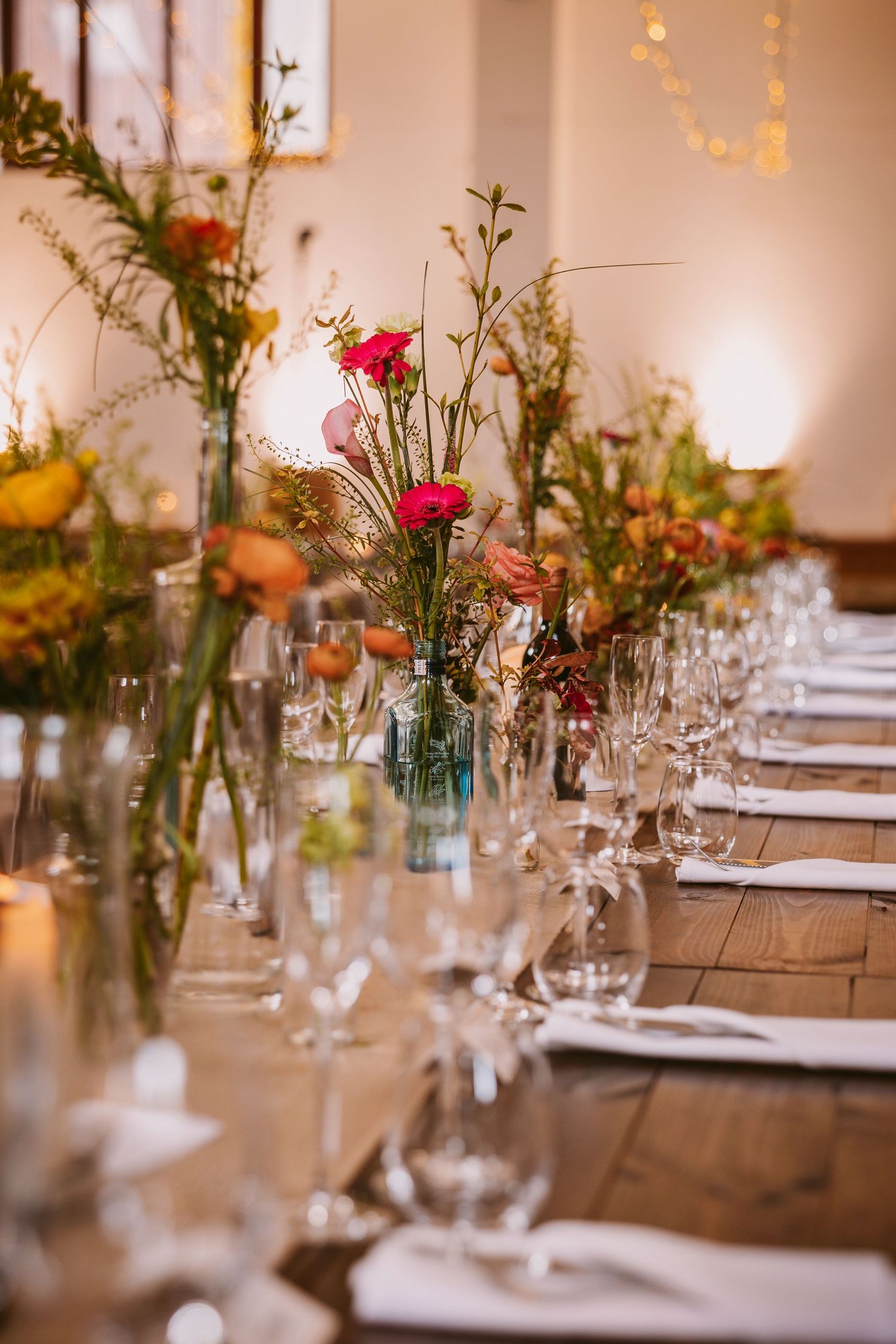 Elegant table settings with rustic glass vases filled with wildflowers and soft lighting for a romantic wedding reception.