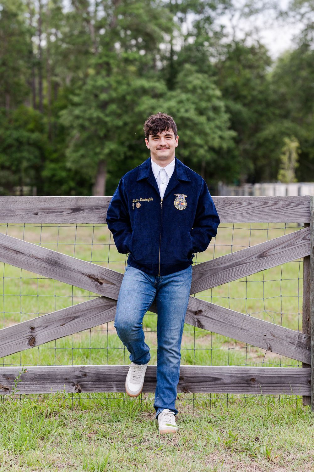 A series of casual poses against a rustic wooden fence in a grassy field with trees in the background.
