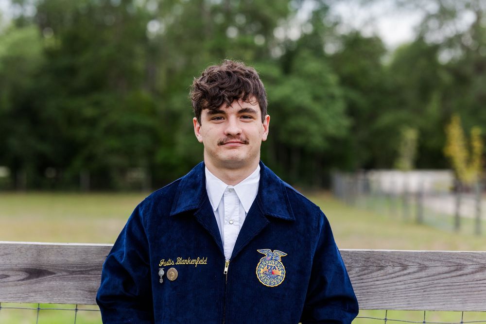 FFA members in blue jackets pose together outdoors on wooden benches during a photo session.