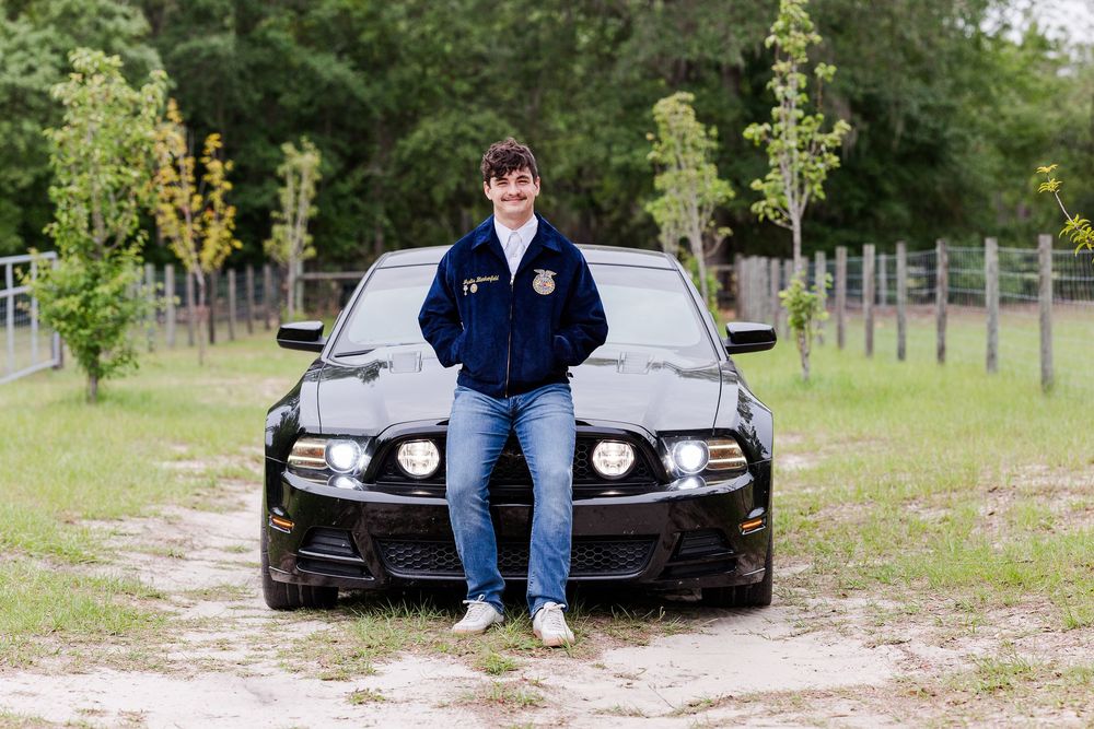 A classic black BMW E30 car parked on a dirt path with trees and grass in the background.