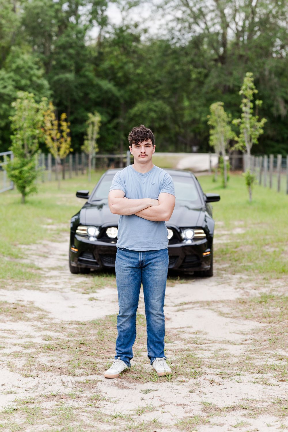A black car parked on a sandy dirt path surrounded by green trees and grass.