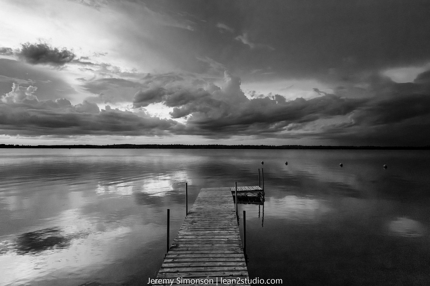 A series of black and white landscape photos showing dramatic cloudy skies over docks extending into calm waters.
