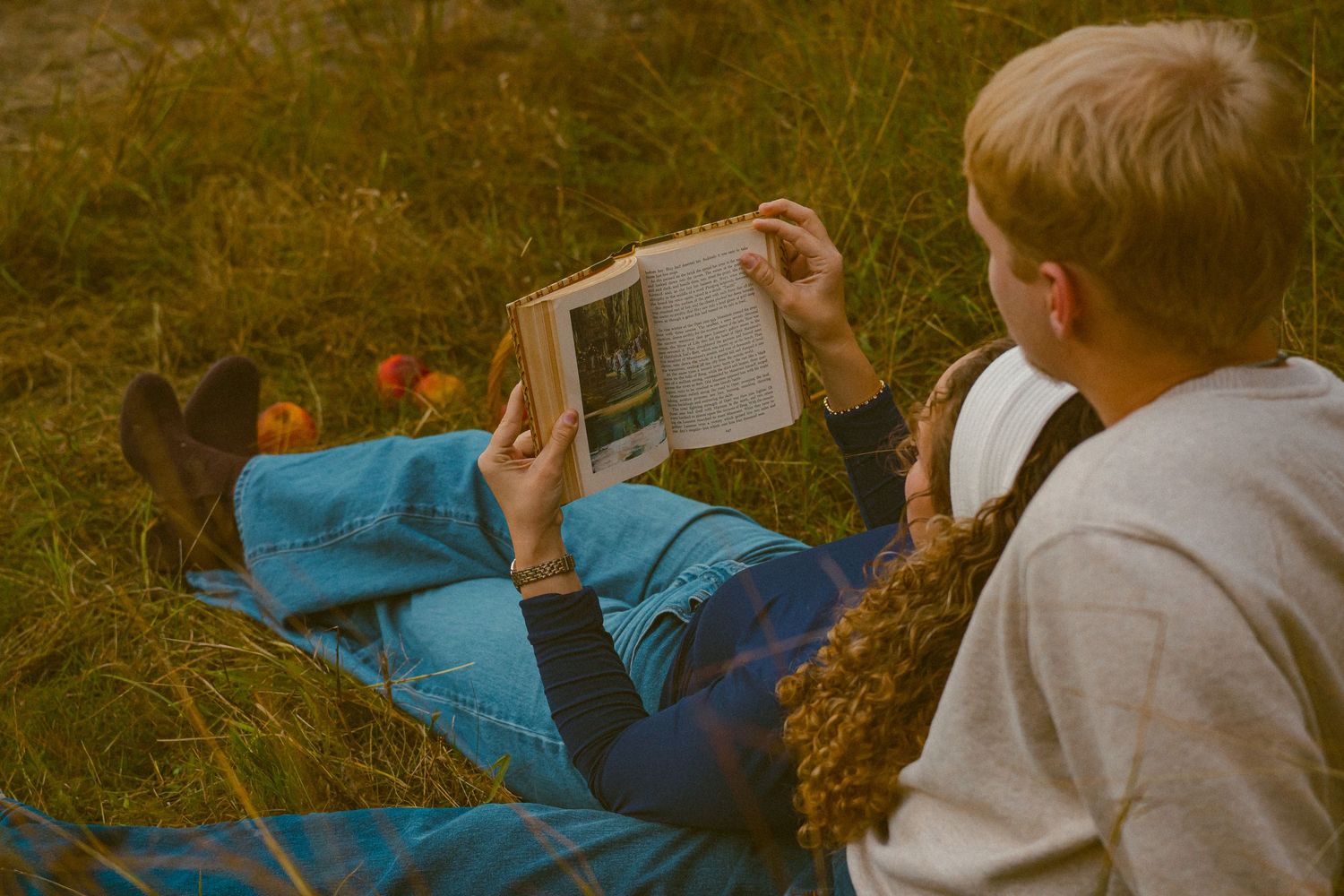 Two people relaxing on grass while reading a book together.