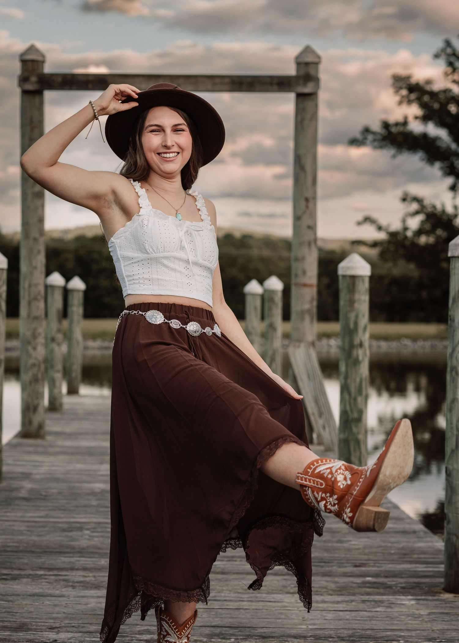 Western style photoshoot on wooden dock with brown skirt and cowboy boots.