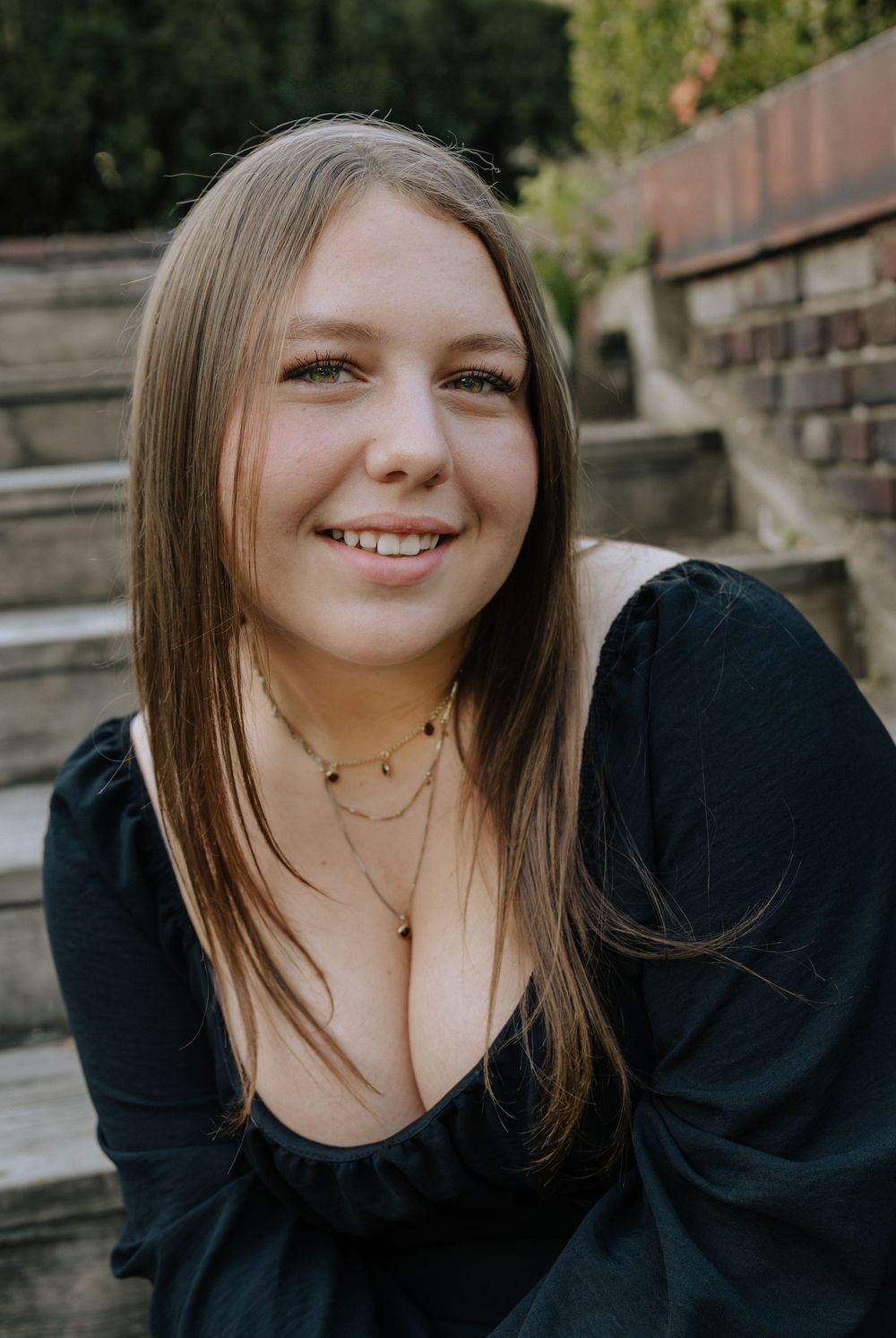 Casual portrait session on stone steps with natural lighting and brick wall backdrop.