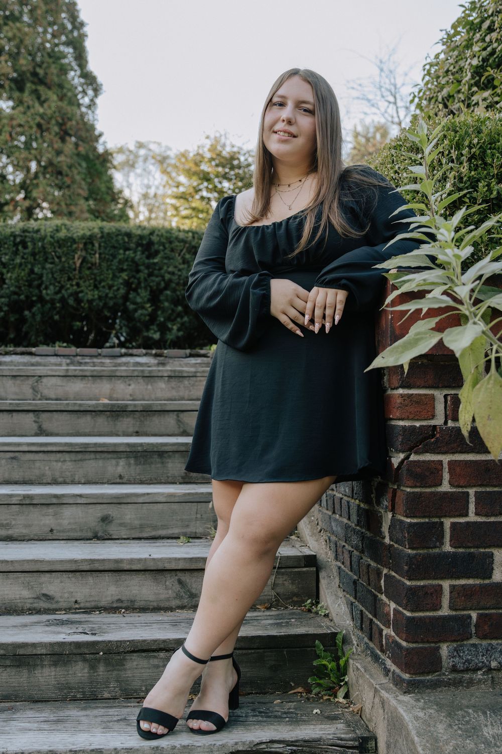 A casual outdoor portrait session featuring someone in a black dress near brick and stone architecture.