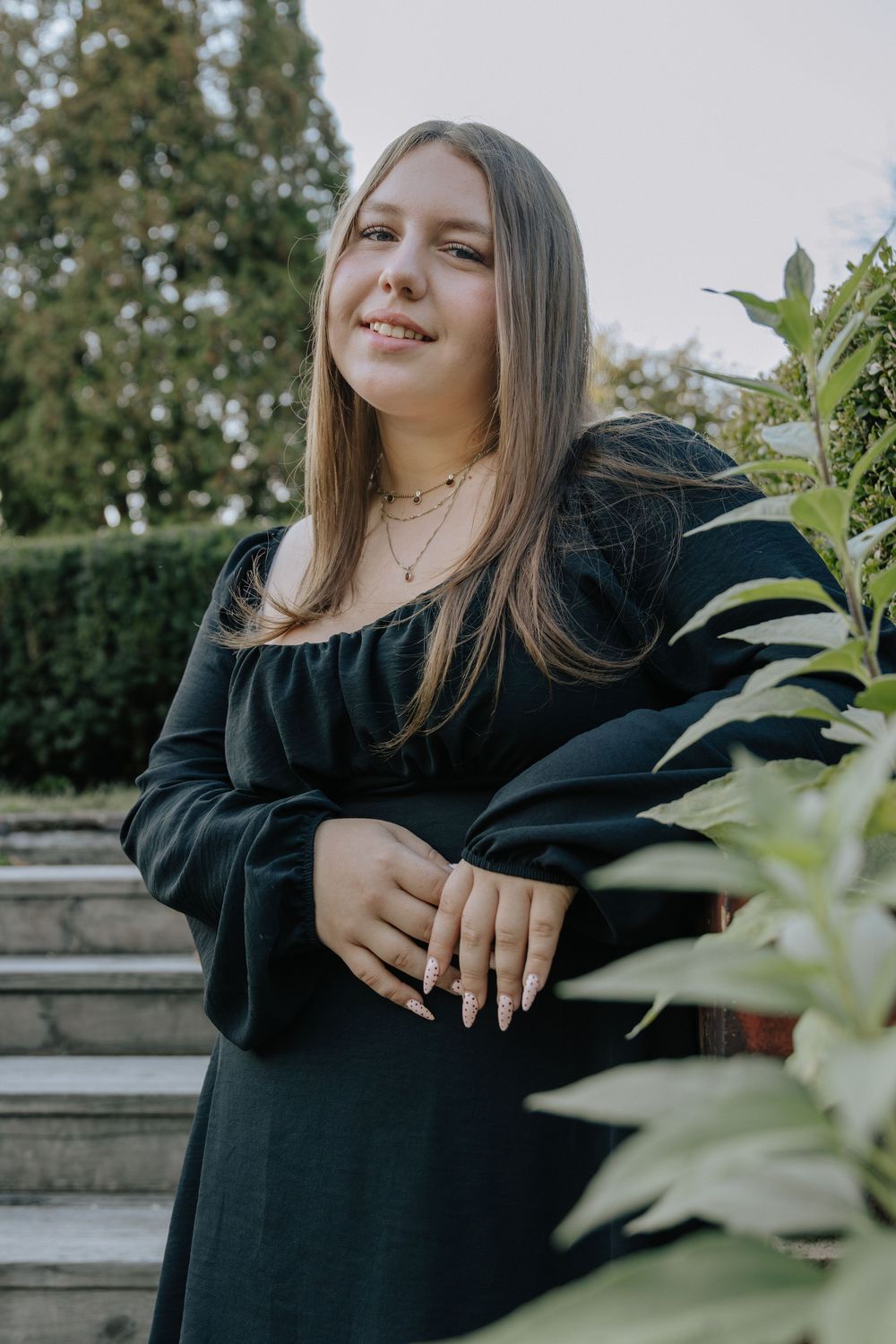 A relaxed outdoor photoshoot with someone wearing black against a natural garden backdrop.