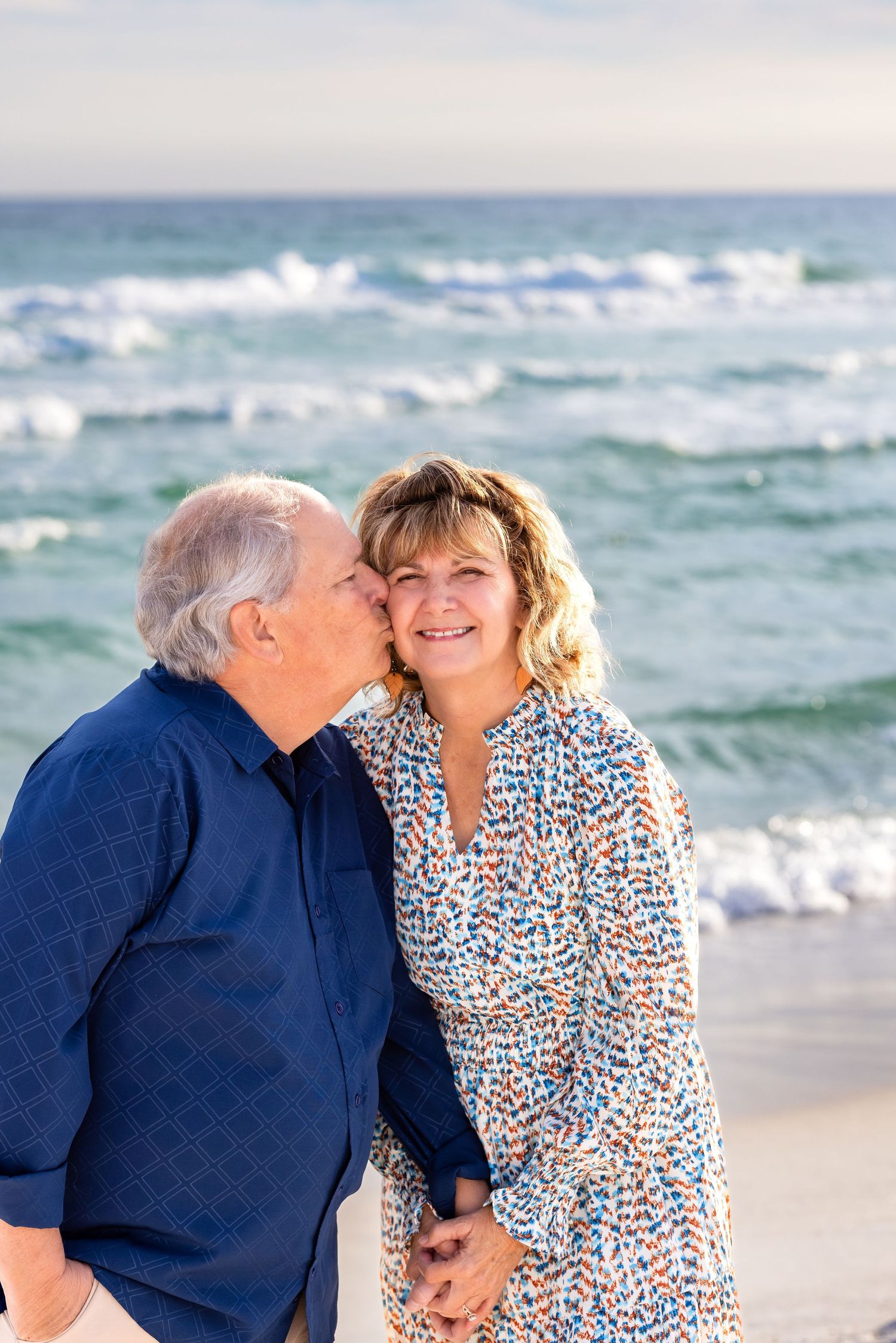 Couple walking along a white sandy beach at sunset with gentle waves rolling onto the shore.
