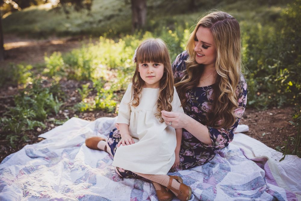 A tender moment captured outdoors on a white blanket amidst natural scenery and warm lighting.