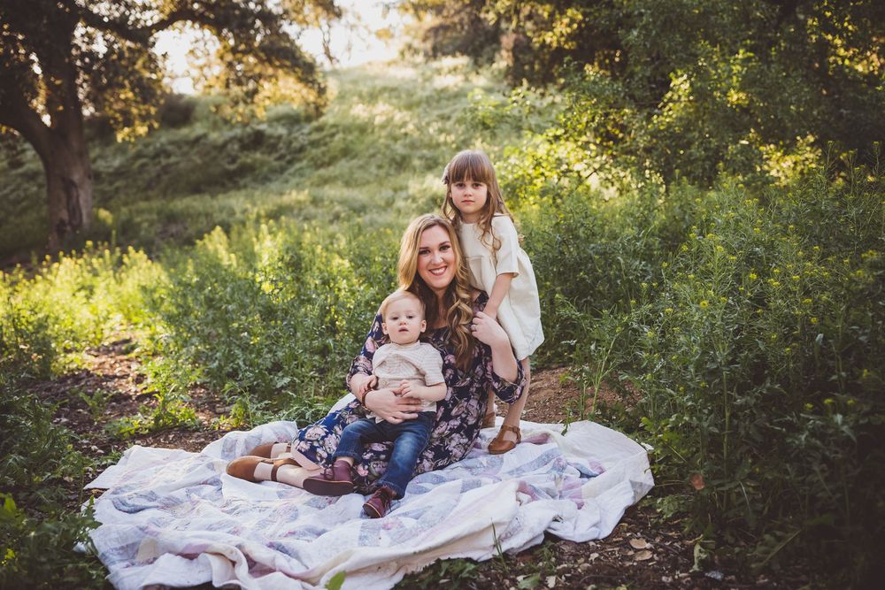 A heartwarming outdoor family portrait on a white blanket surrounded by lush greenery at golden hour.
