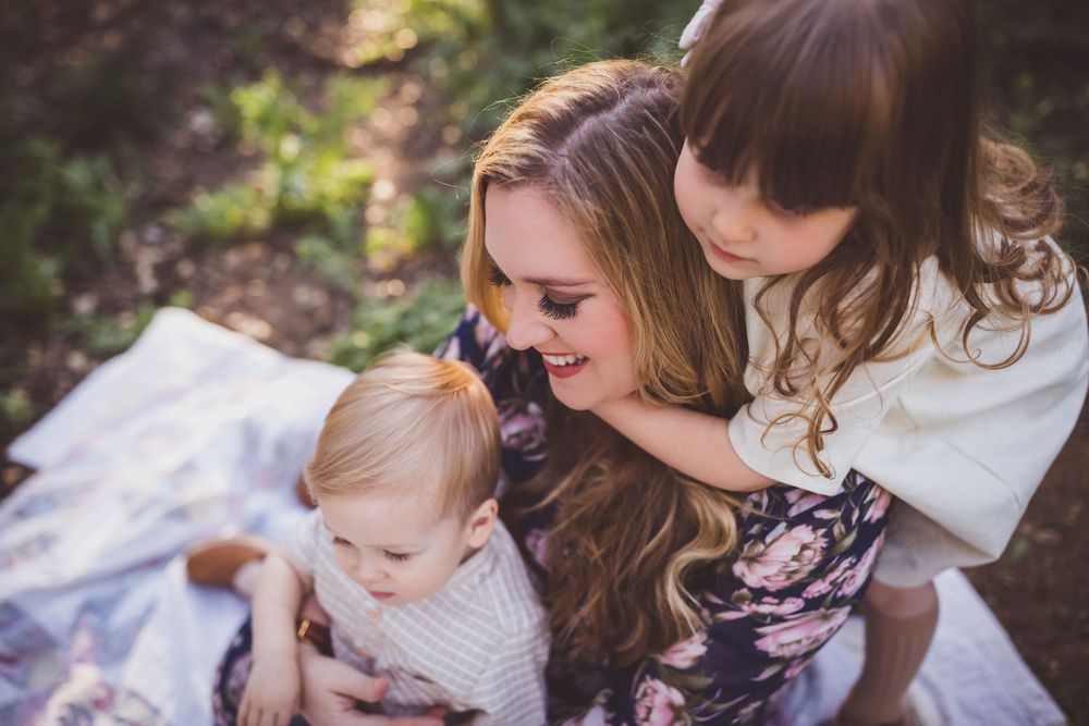 Three people share a joyful moment together while sitting on a white blanket outdoors.