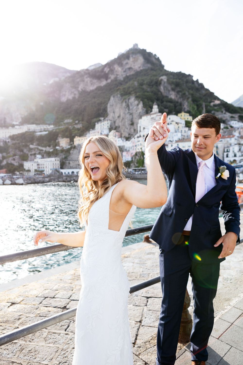 A couple celebrates their elopement wedding day in Amalfi at the coast with mountains and village buildings in background.