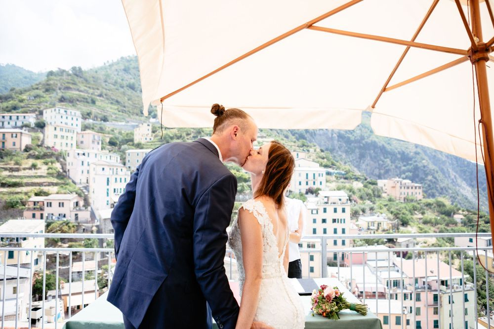 A romantic kiss during a wedding ceremony overlooking the stunning hillside buildings of Riomaggiore along the coast of the Cinque Terre.