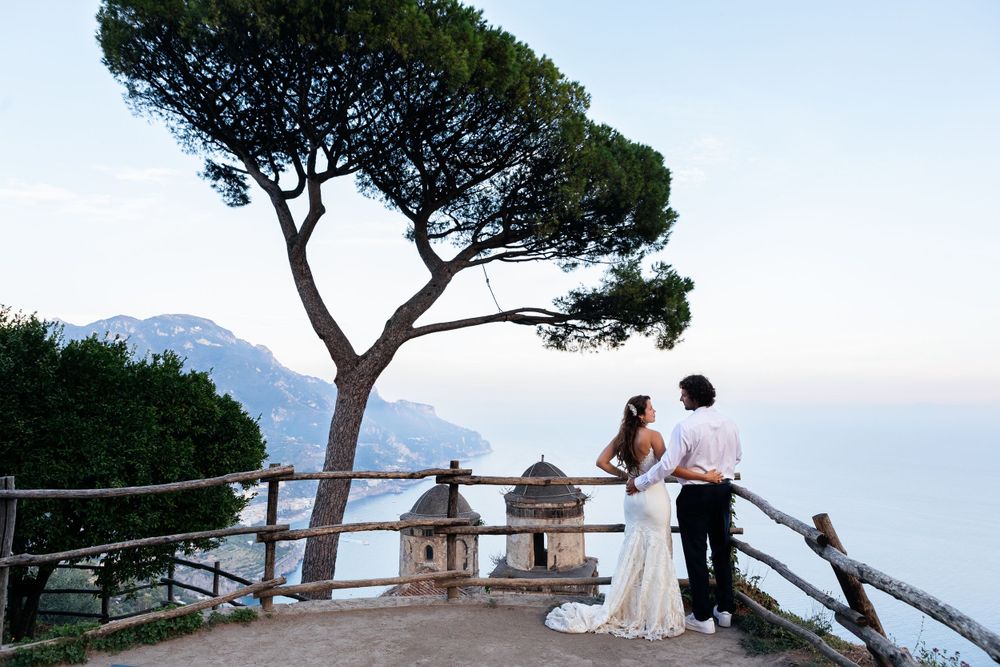 A couple elope and share a romantic moment at Villa Rufolo in Ravello, Italy with a scenic Amalfi Coast view behind them.