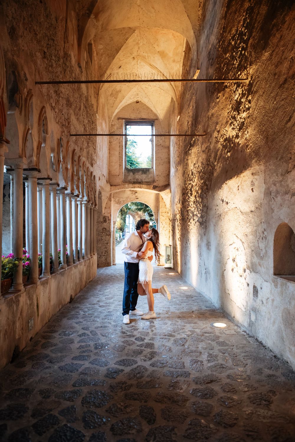 A couple embraces in a romantic moment under the arched stone colonnade at Villa Rufolo in Ravello during their elopement in Amalfi.