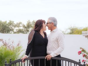 A couple shares an intimate moment on a balcony with white walls and red flowers.