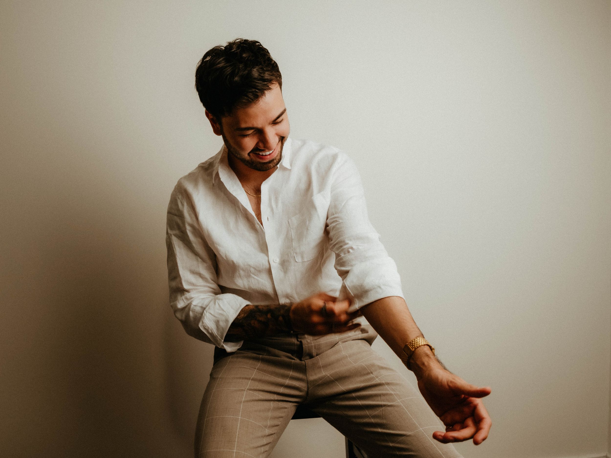 A person in a white button-down shirt and khaki pants poses against a light colored wall.