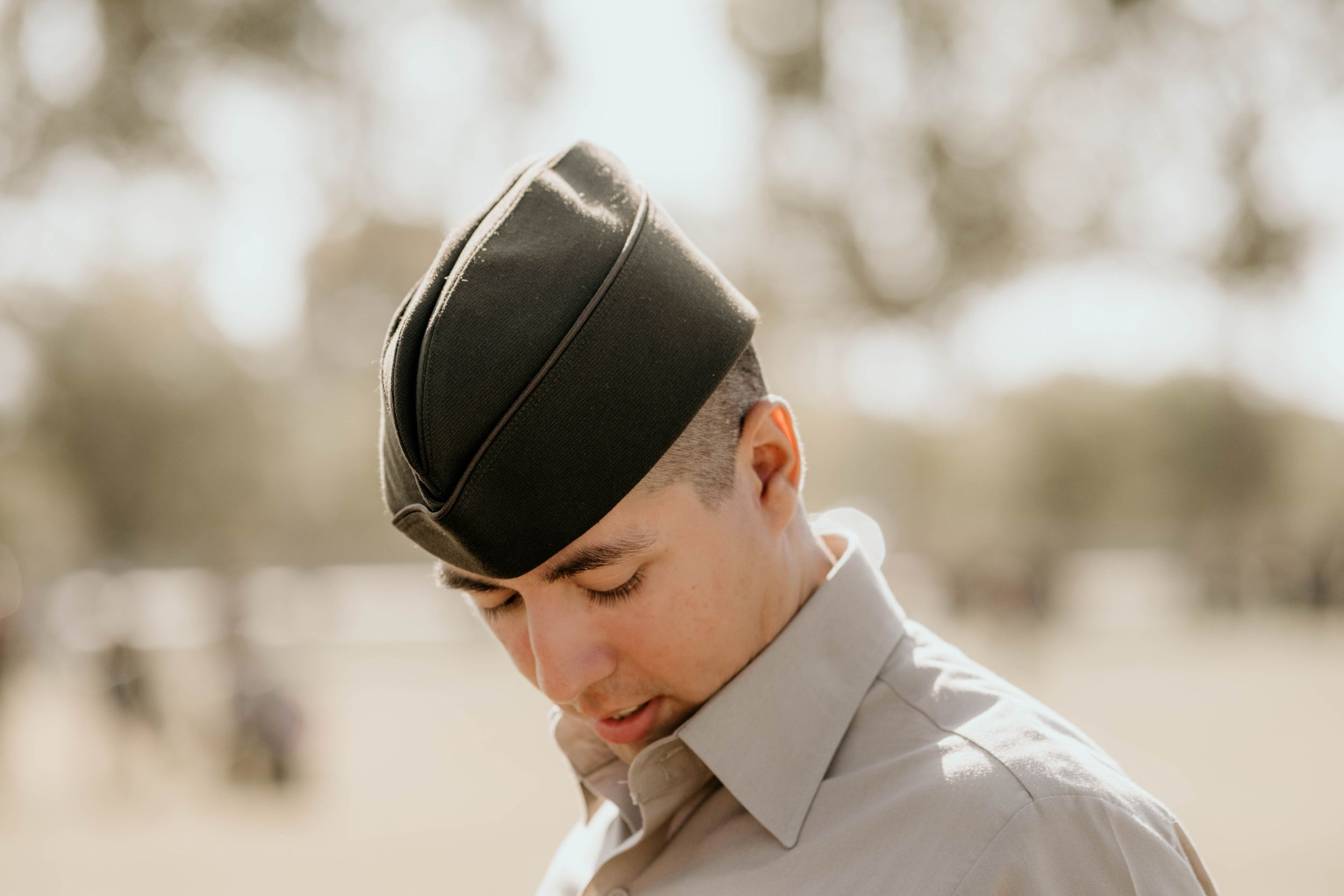 A military service member in dress uniform and cap looking down contemplatively.