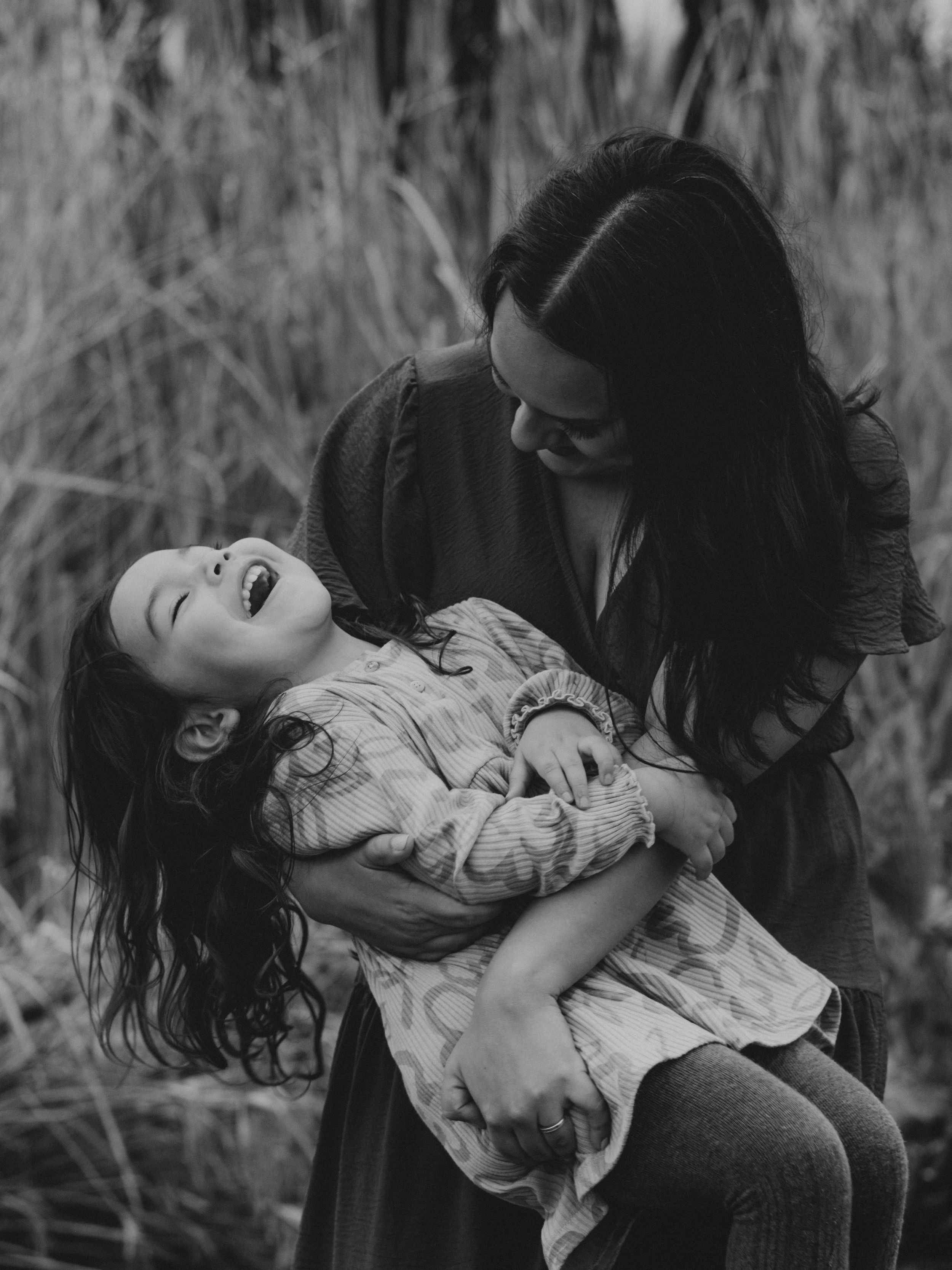 A touching black and white portrait of playful moments between parent and child in tall grass.