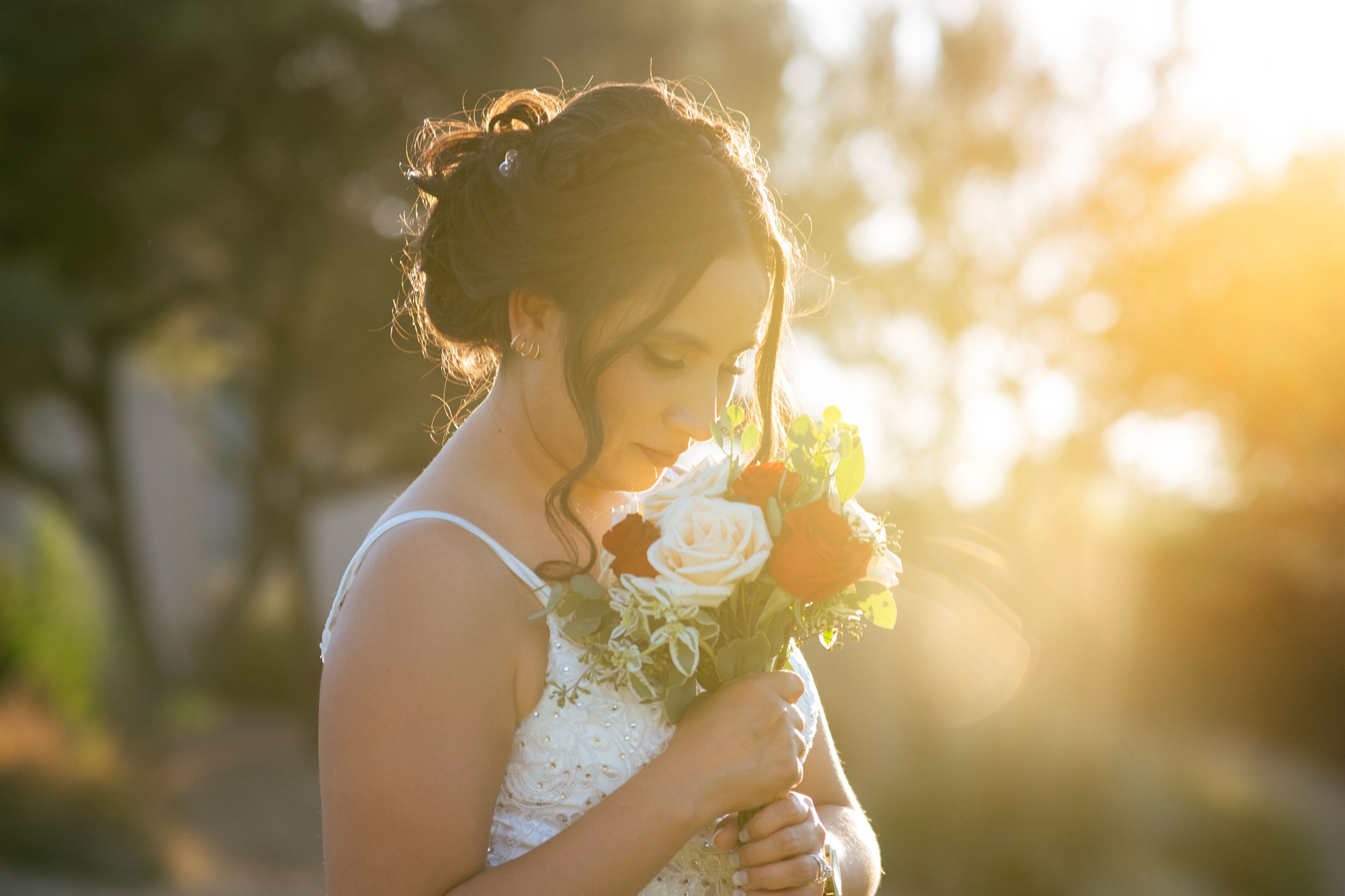 A bride holds a white bouquet during golden hour sunset.
