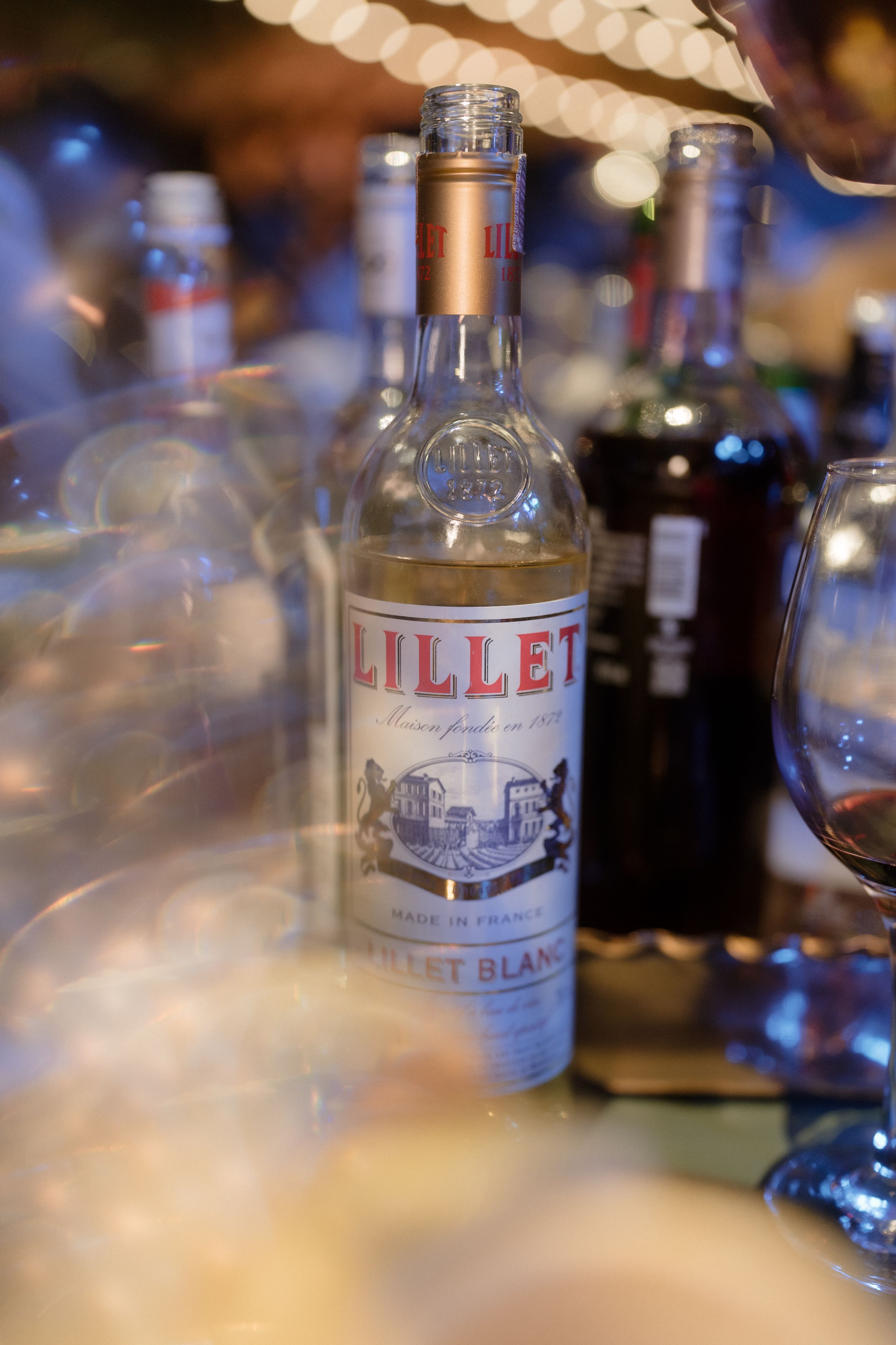 Close-up shot of a Lillet Blanc bottle with bokeh lighting effects in background.