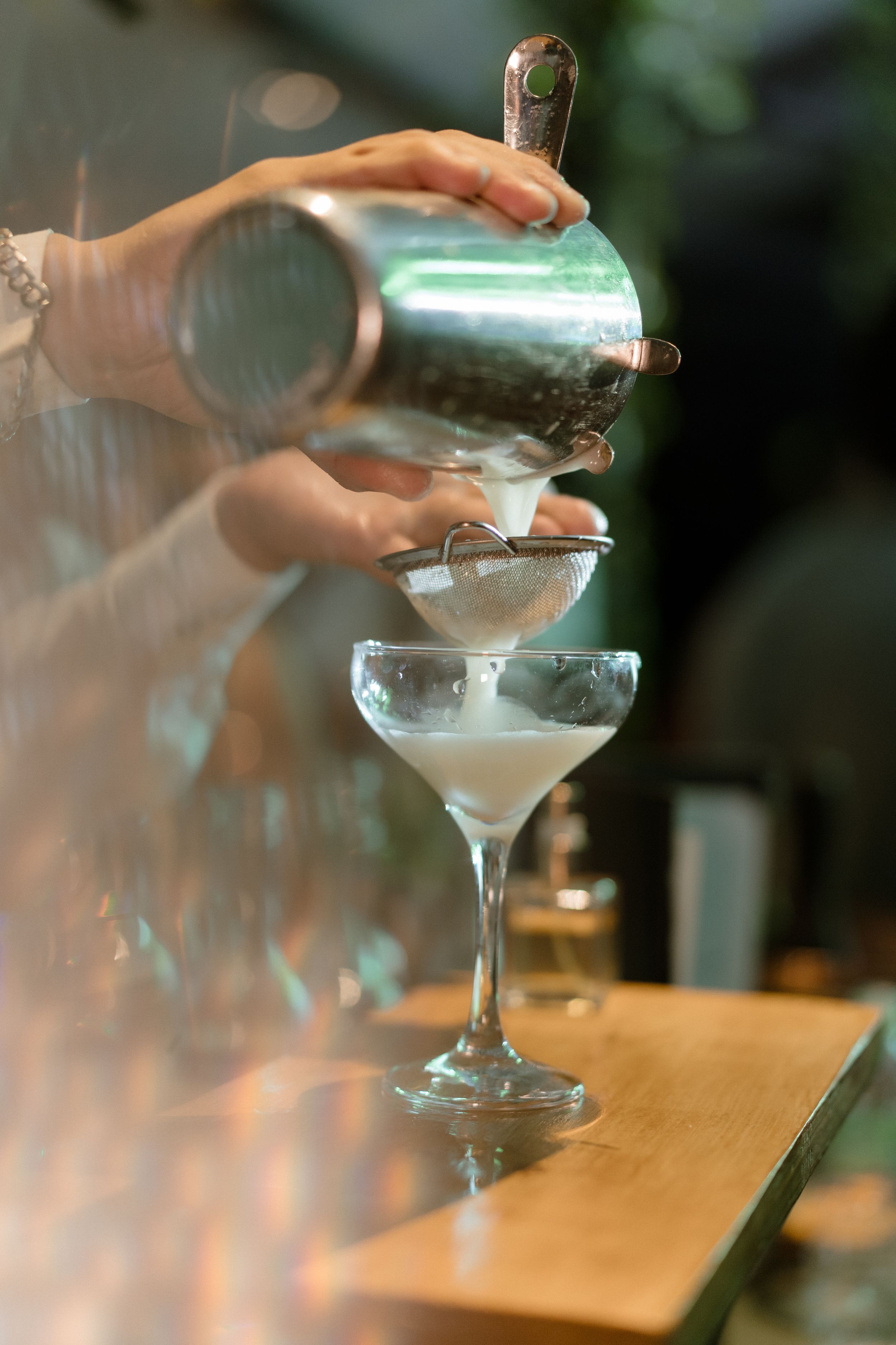 Bartender pouring a smoky craft cocktail into a martini glass.