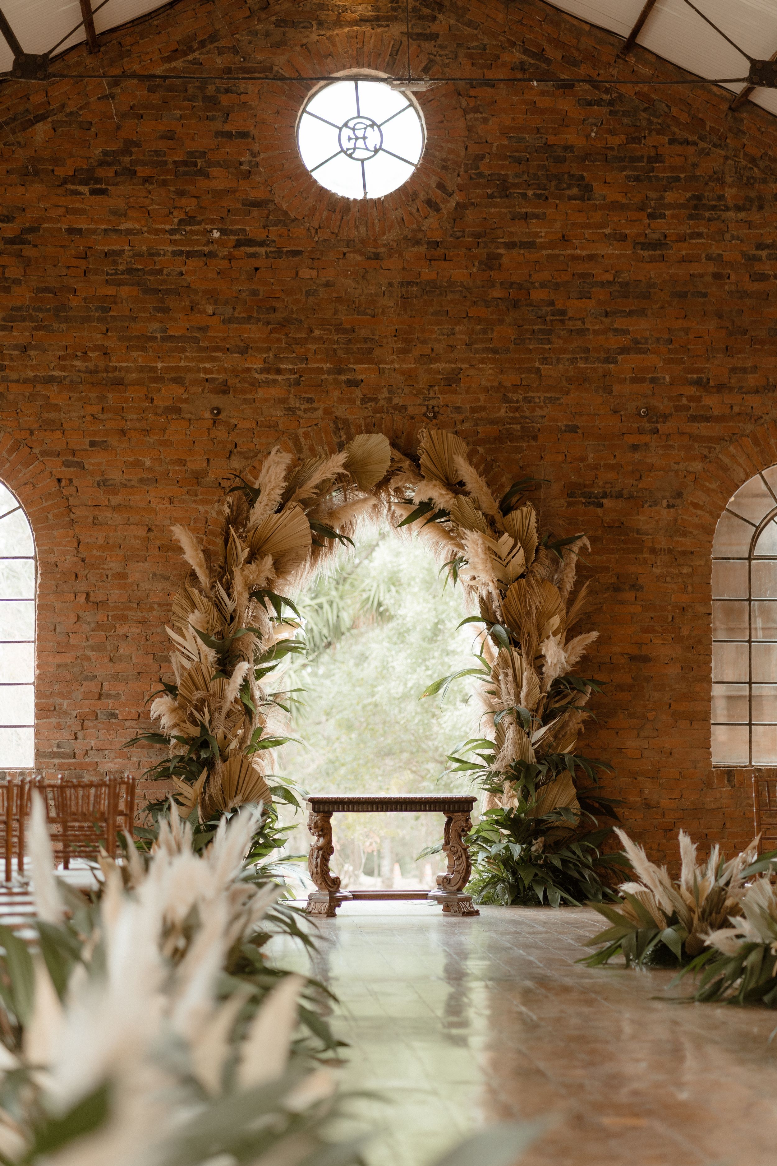 A rustic brick chapel interior with a round window and floral arch for a wedding ceremony.