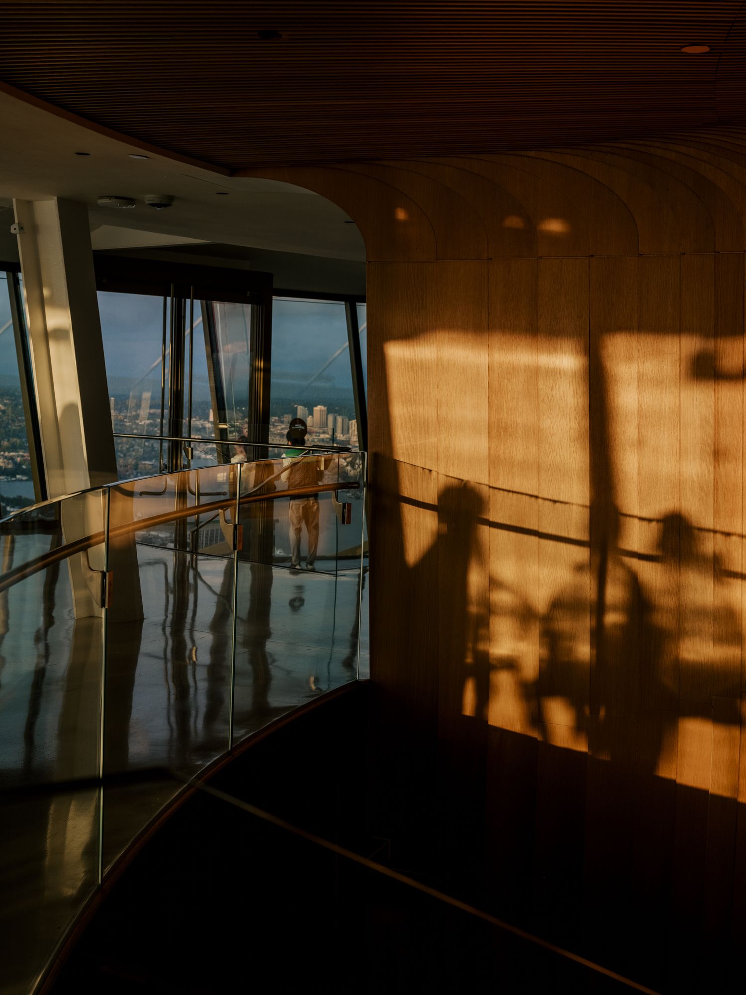 Warm sunlight casts dramatic shadows across a modern high-rise interior space with reflective floors and city views.