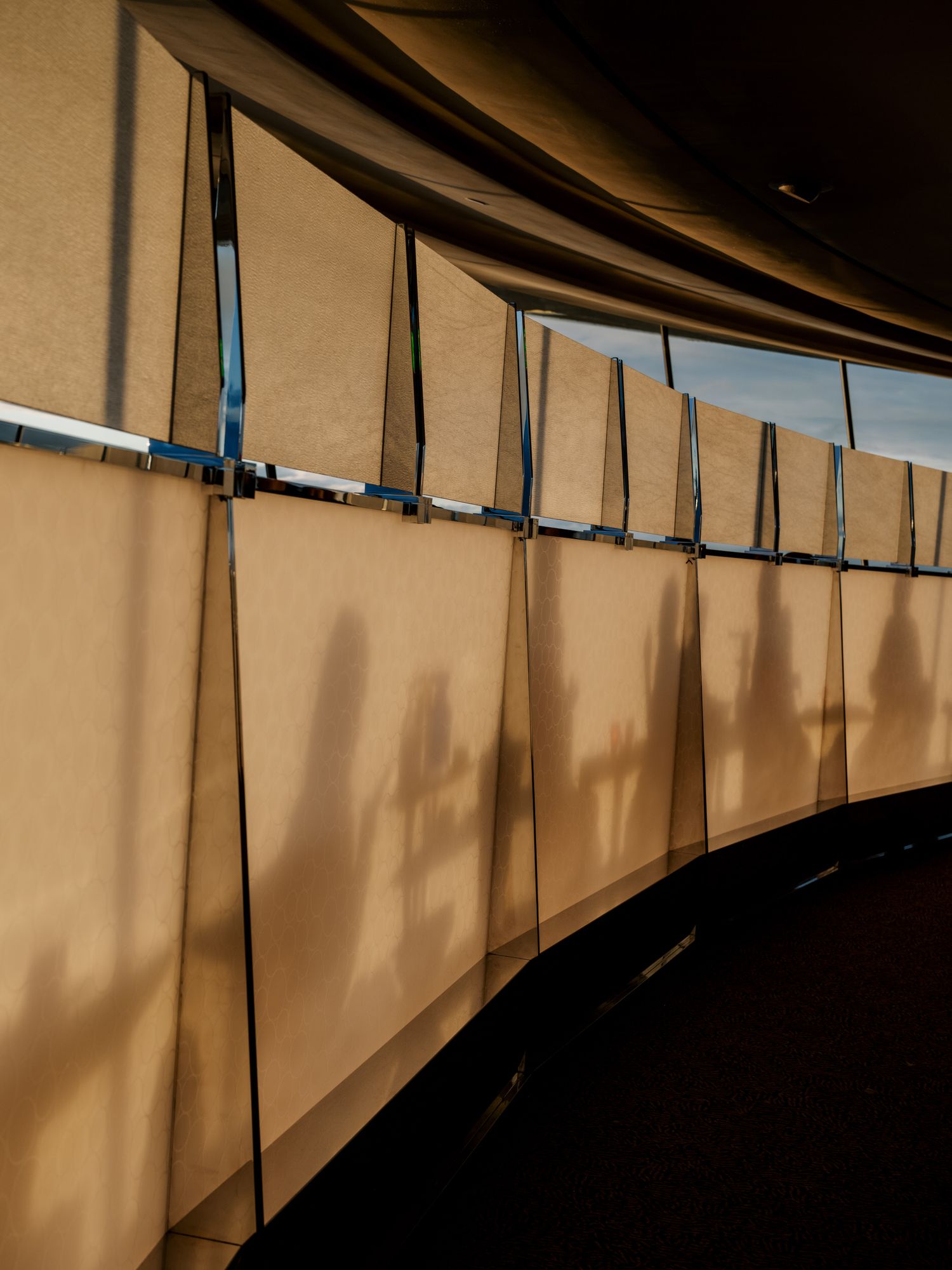Curved beige wall with vertical metal supports casting dramatic shadows in a modern architectural passageway.