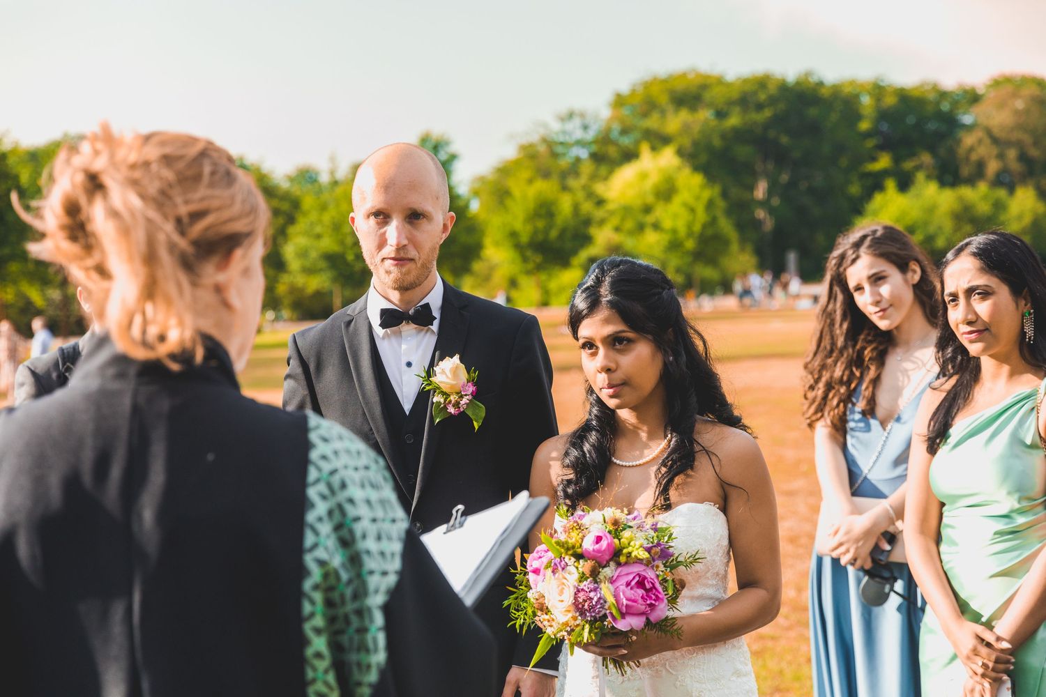 An outdoor wedding ceremony in progress with guests and officiant on a sunny day.