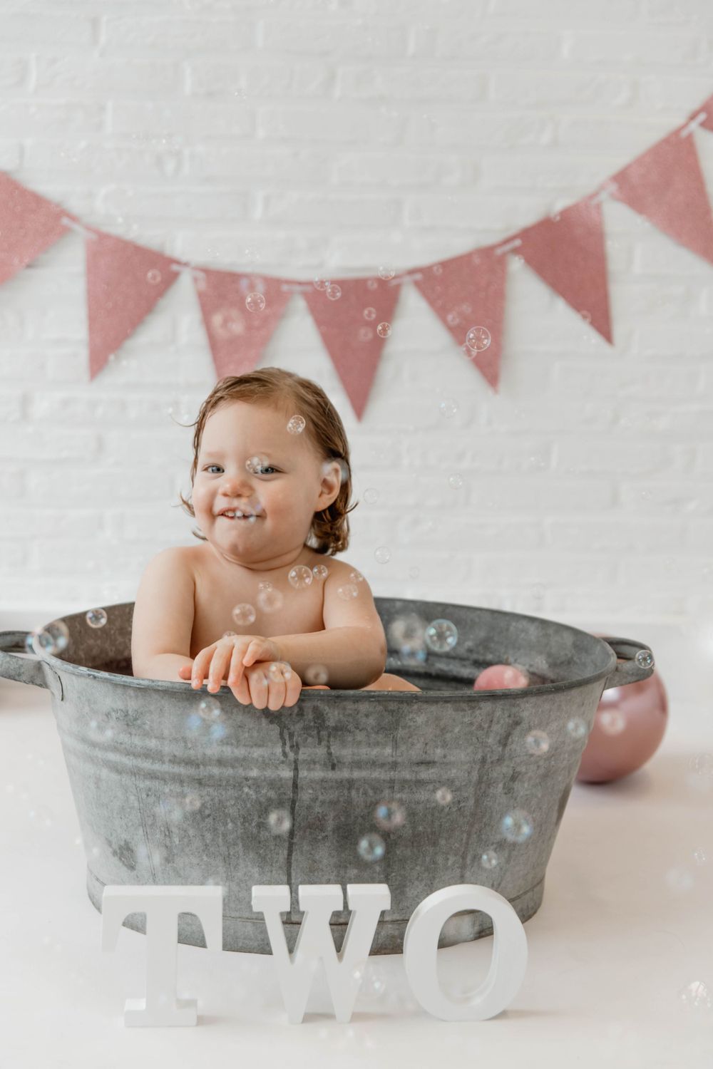 Child having fun in metal bathtub with pink banner decoration.