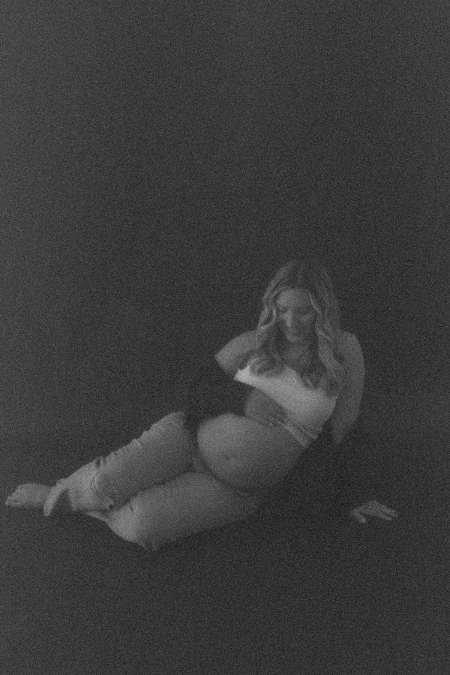 Moody black and white maternity portrait in a dark studio setting.
