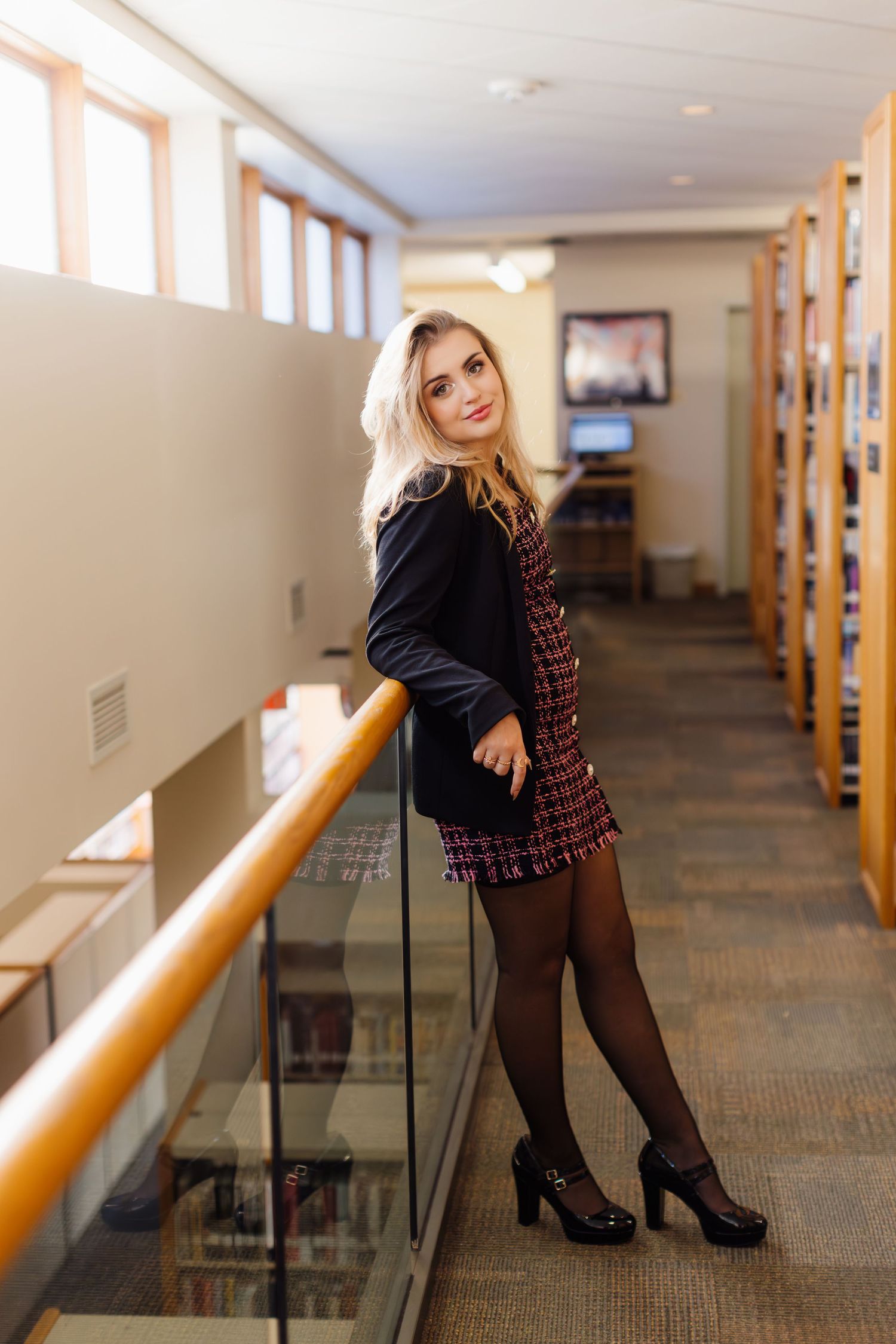 Someone stands in a library hallway wearing a black top and plaid dress with tights and heels.