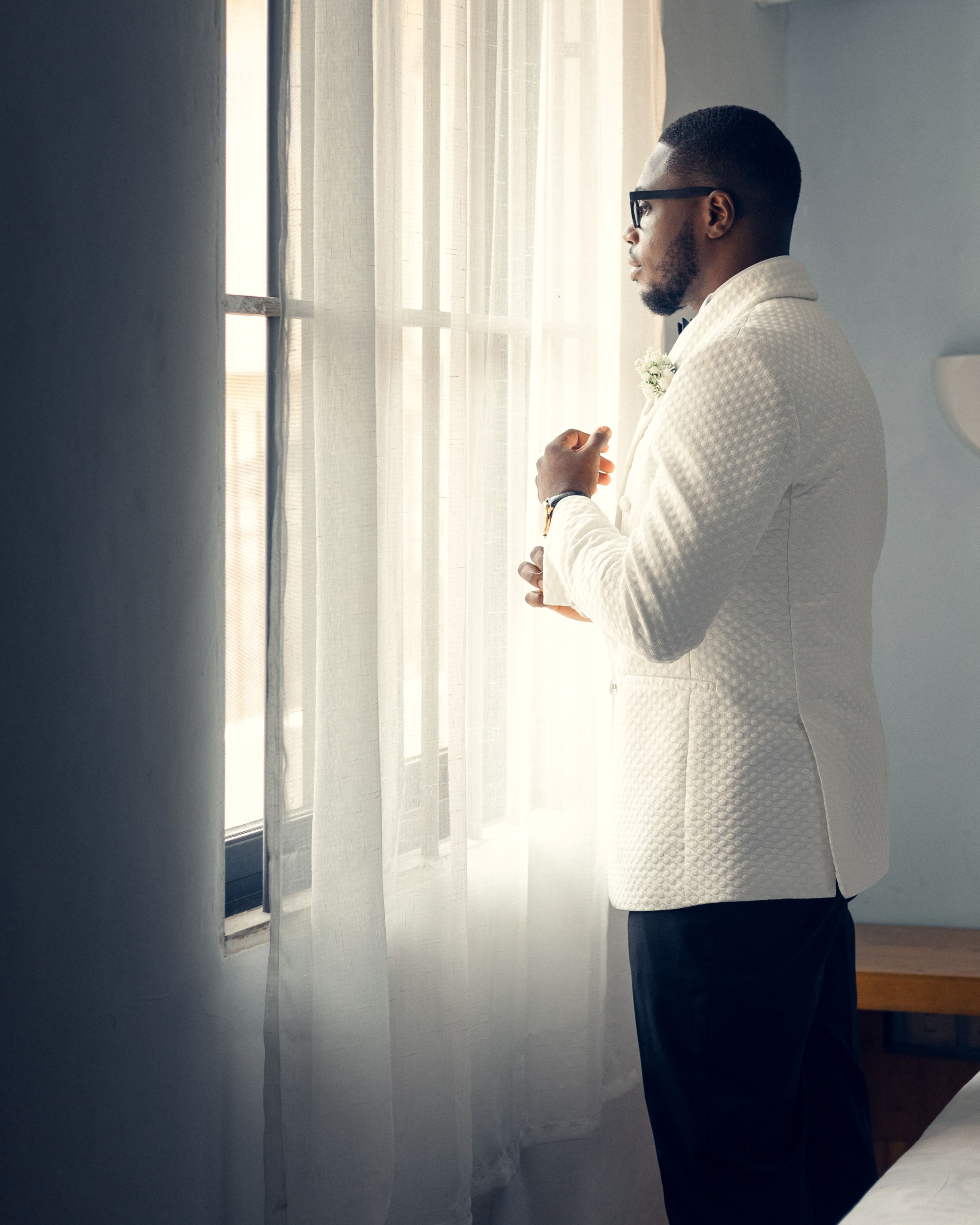 Side view of groom in white textured jacket gazing out window.