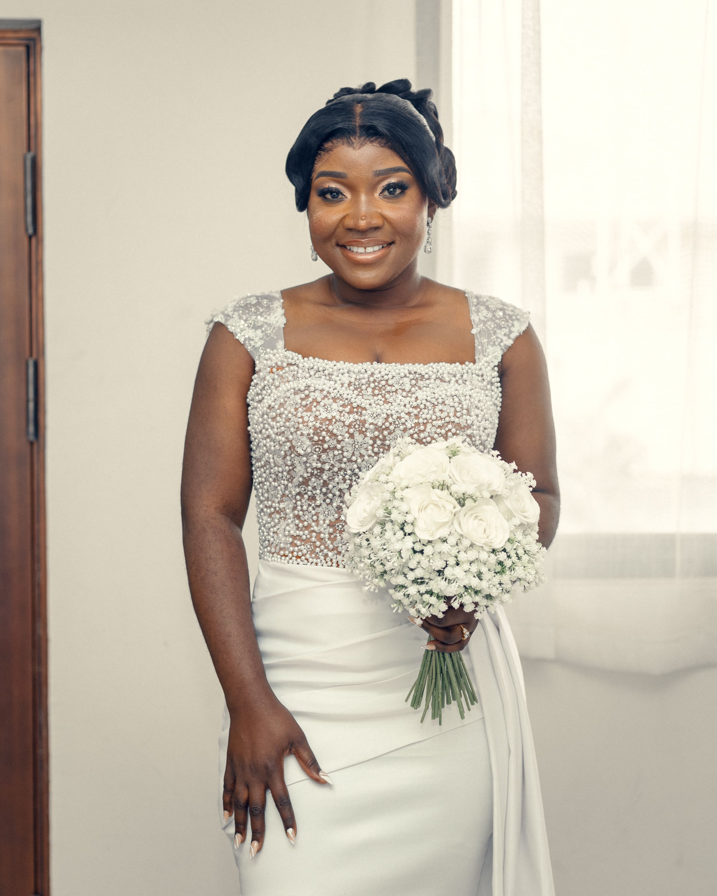 A bride in an elegant beaded white wedding gown with cap sleeves holds a white bouquet.