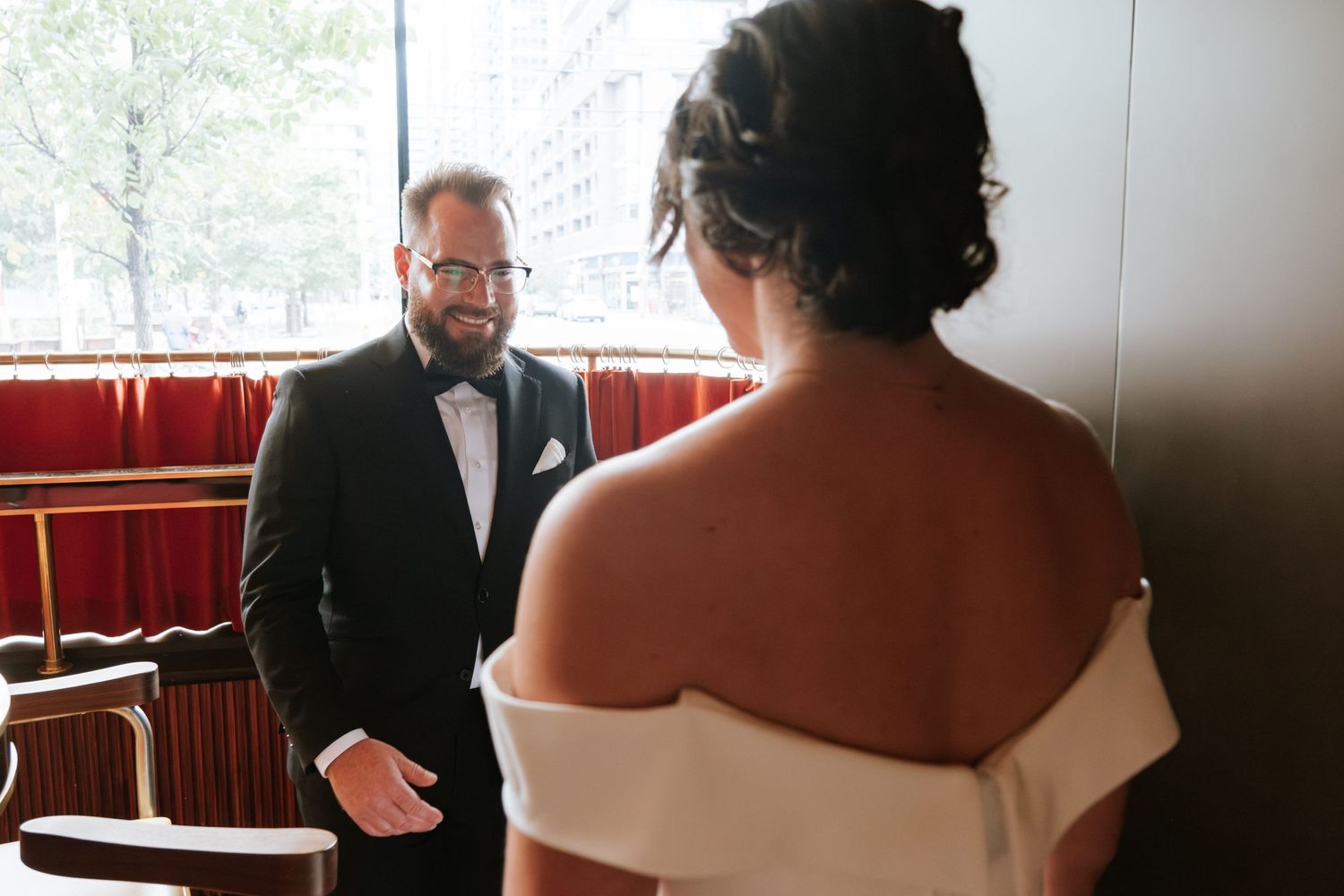 Wedding first look moment captured in venue with red booth seating.