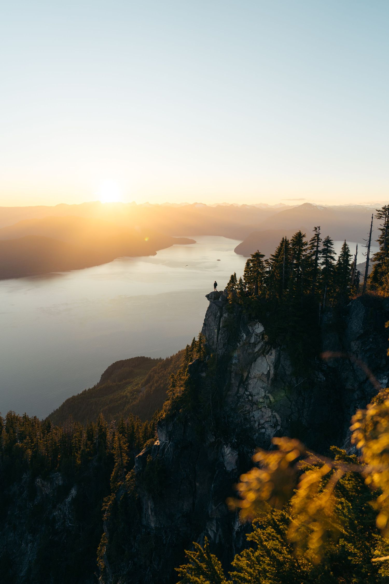 Scenic mountain overlook at sunset with dramatic cliffs and a lake view below.