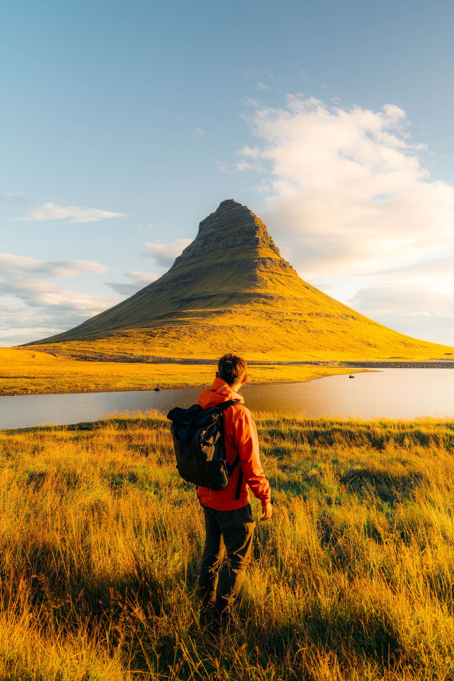 Photographer silhouetted against golden grasslands capturing iconic Kirkjufell mountain in Iceland at sunset.