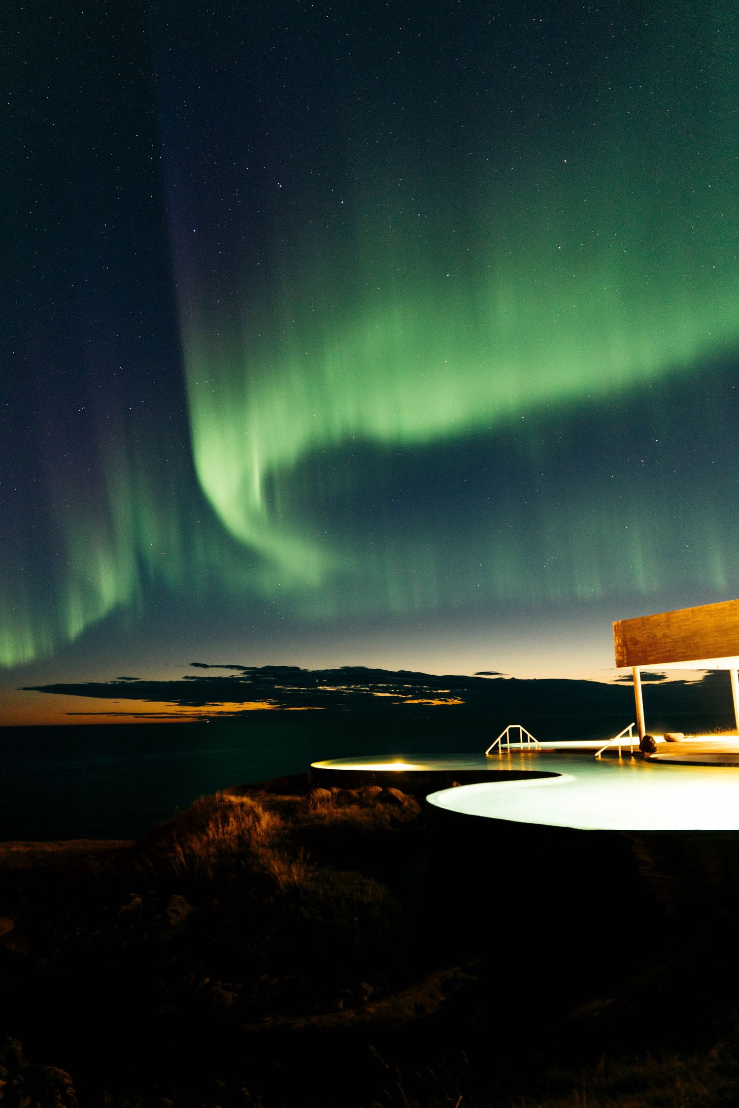 Stunning green aurora borealis lights dance across night sky above illuminated coastal building in Iceland.