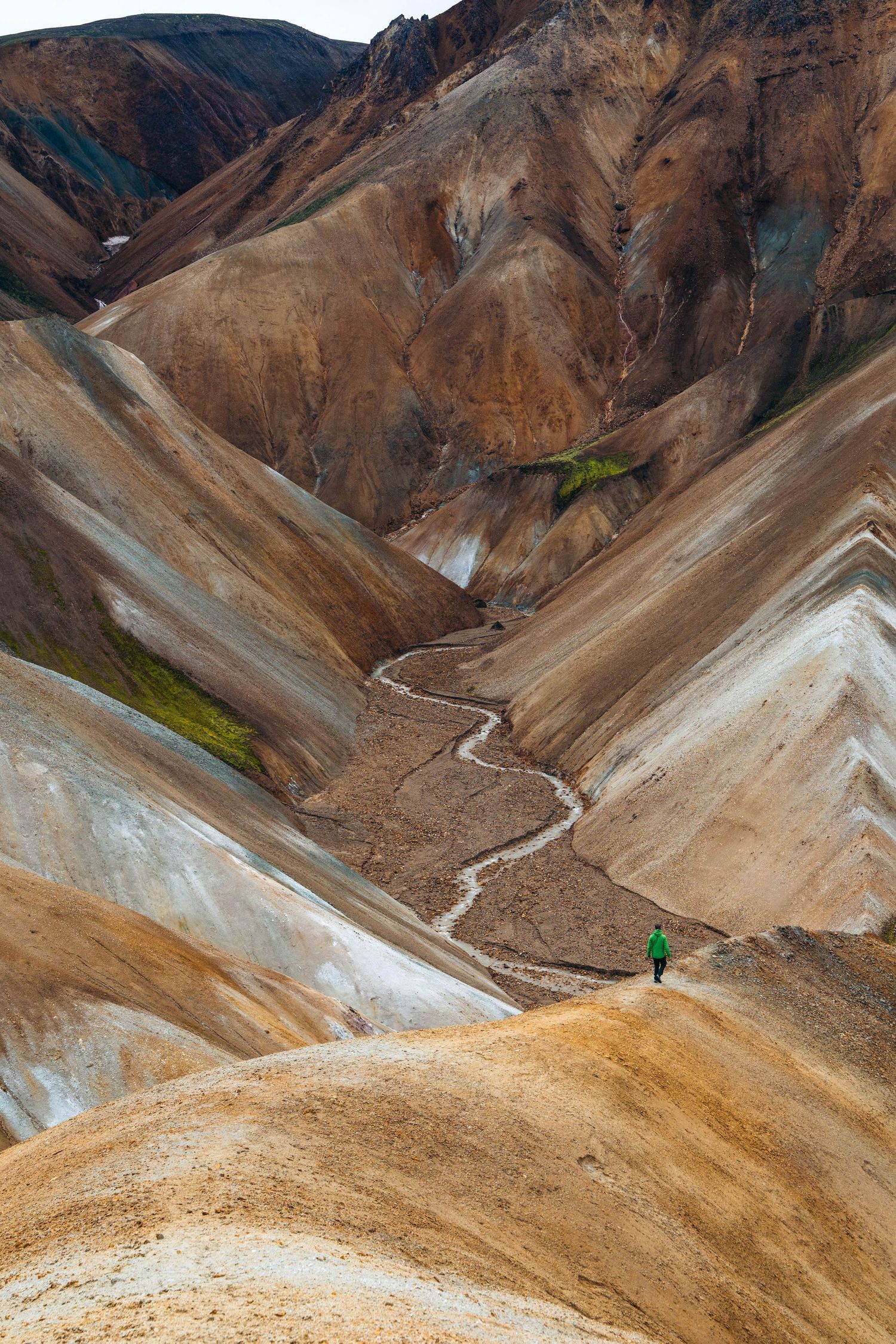 A winding mountain trail cuts through colorful layered hills in Landmannalaugar, Iceland's rugged volcanic landscape.