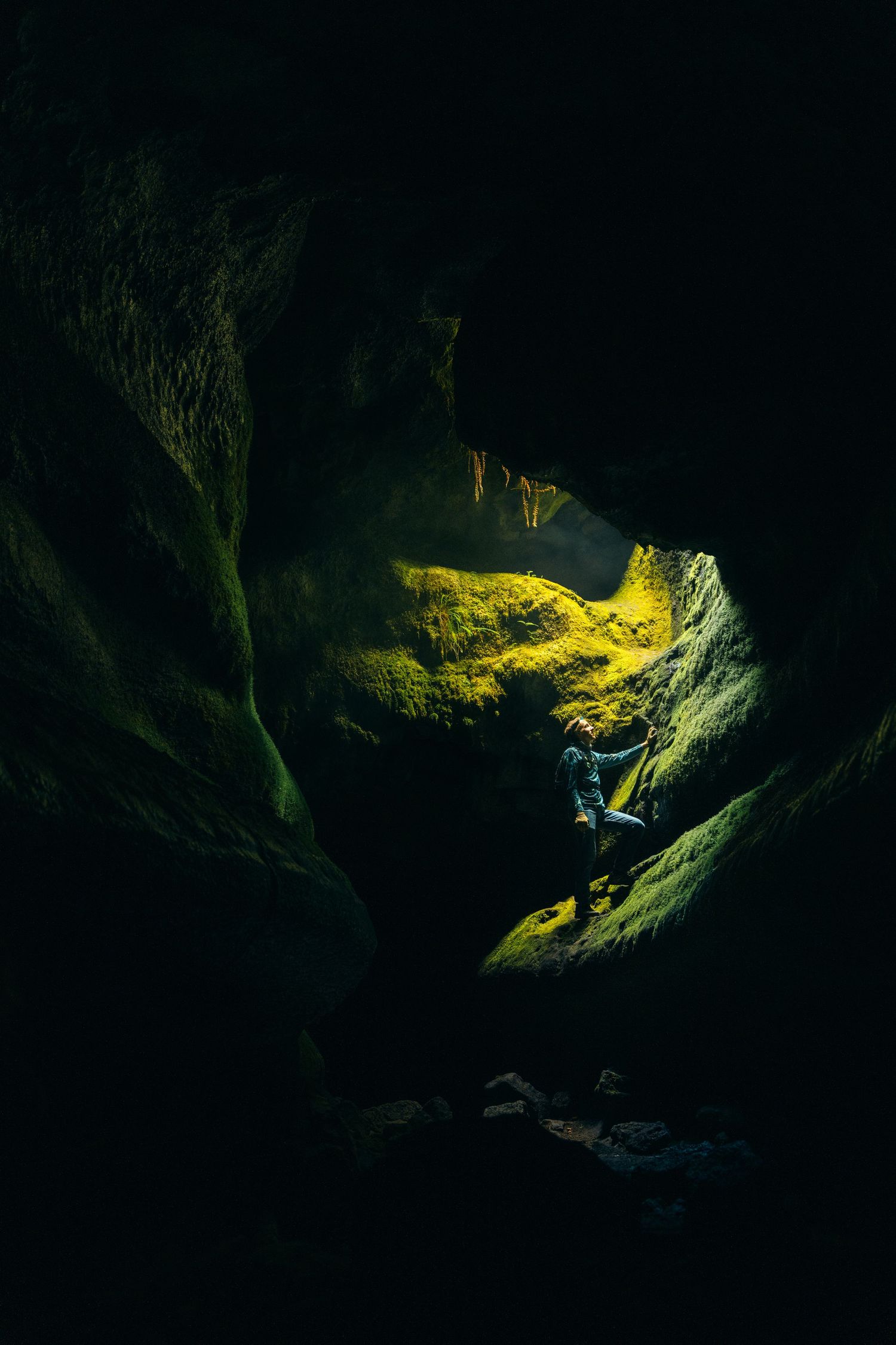 Explorer illuminated by spotlight in dark cave chamber with golden rock formations.