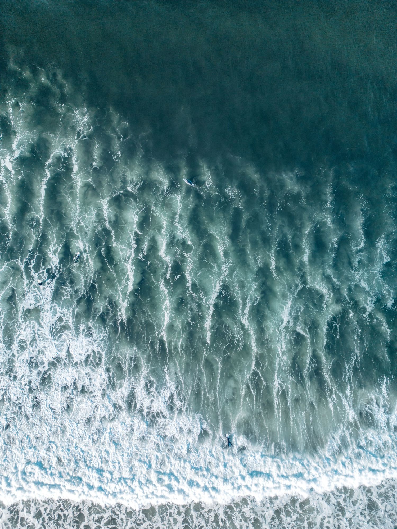 Aerial view of rolling ocean waves creating natural patterns where they meet the shore.